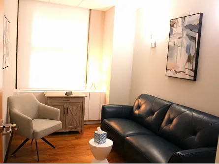 A bright consulting room with a black sofa and two chairs
